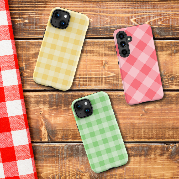 Gingham phone case collection image featuring yellow, green, and pink styles on a rustic wood background for the Stay In Your Grid Era drop by Ninja Level Designs